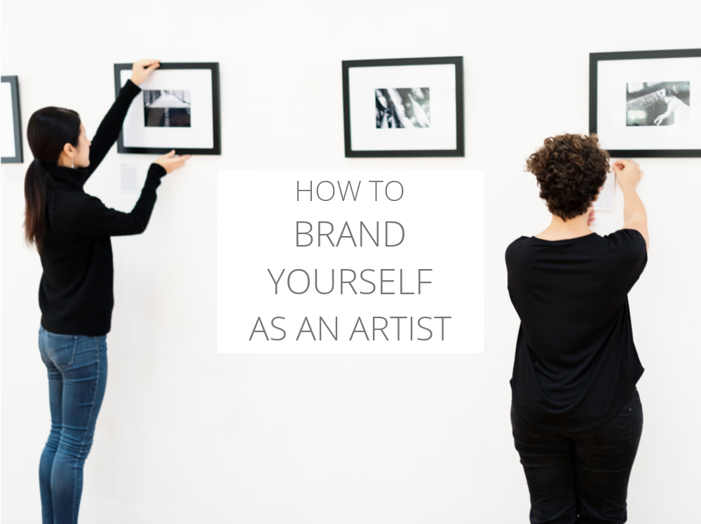 Two women hanging art on a gallery wall | How to brand yourself as an artist.